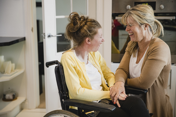 Female in yellow in wheelchair with another female holding her hand.