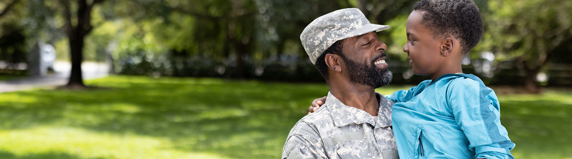 Black Veteran in Army fatigues carrying his son and smiling at him